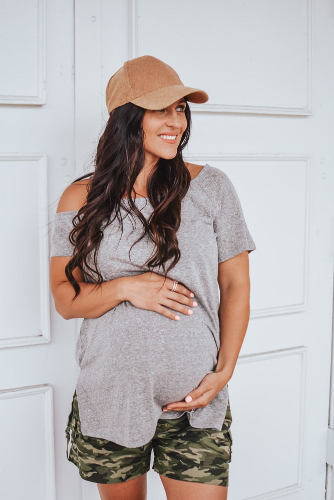 maternity outfit ideas - woman in baseball cap, shirt, and shorts