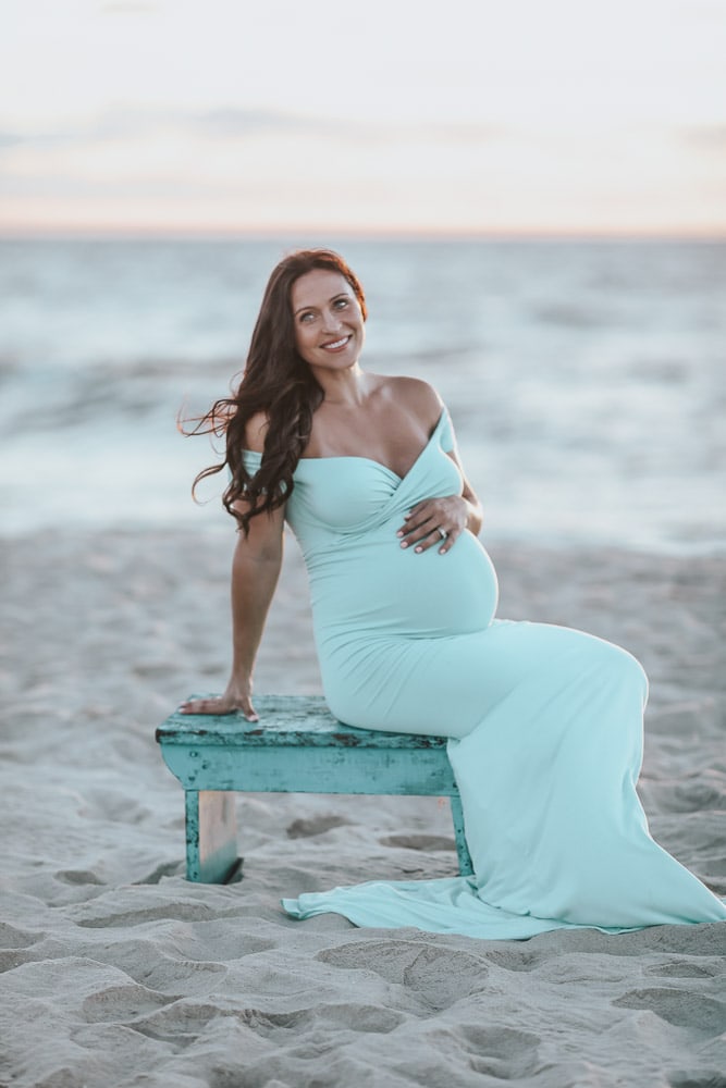 pregnant woman sitting on bench during a beach maternity photoshoot