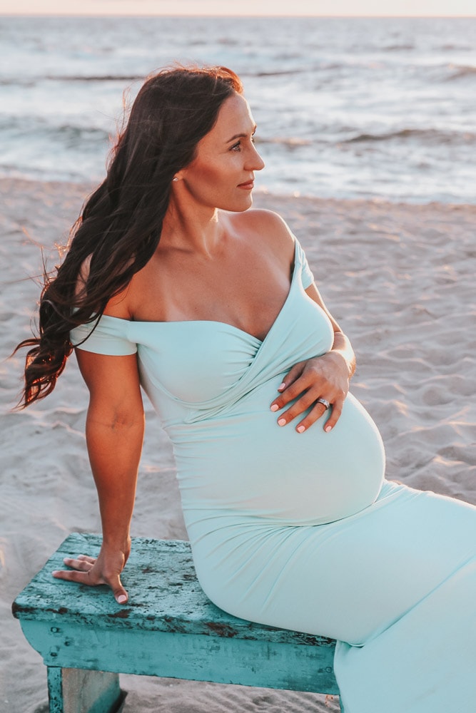 woman sitting on a bench during a beach maternity photoshoot