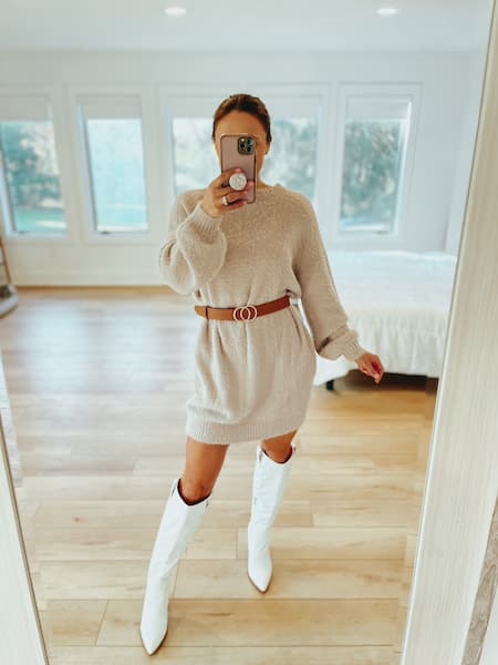 a woman wearing a beige sweater dress with a tan belt and white cowboy boots.