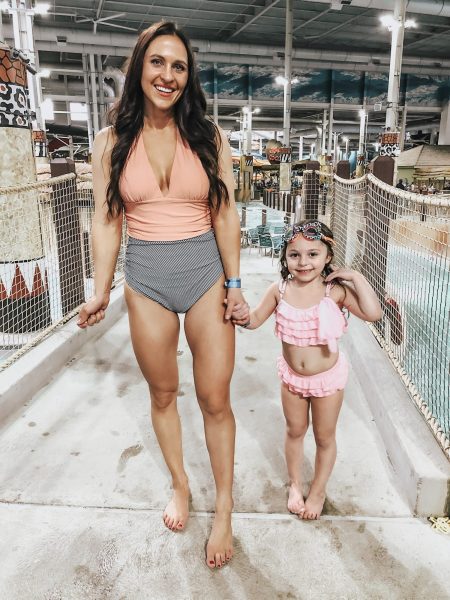 A woman in a plungeline halter one-piece bathing suit and a girl in a pink bikini.