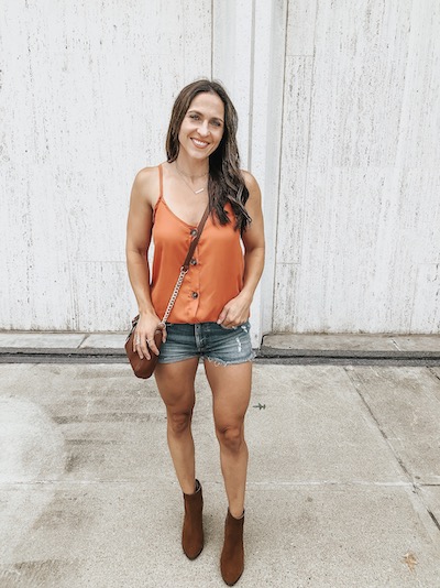 a woman wearing an orange button down cami, denim shorts, and brown booties