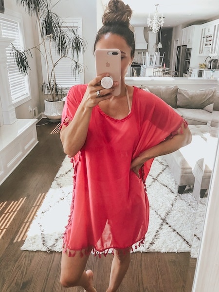 A woman taking a mirror selfie wearing a pink swimsuit cover up.