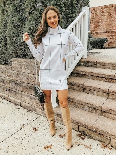 A woman wearing a white and black sweater dress with tan knee high boots.