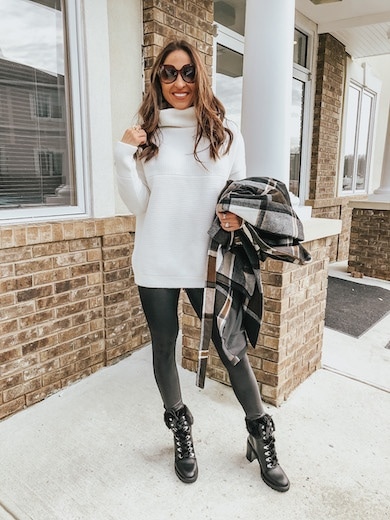A woman wearing black faux leather leggings, a white turtleneck sweater, and black combat boots. 