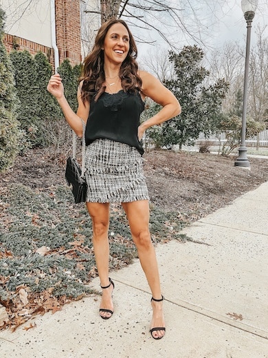 A woman wearing a tweed mini skirt and black tank top with black ankle strap heels.