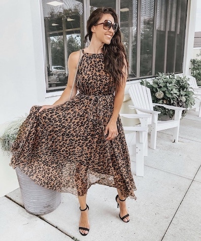 A woman wearing a leopard maxi dress with black ankle strap heels.