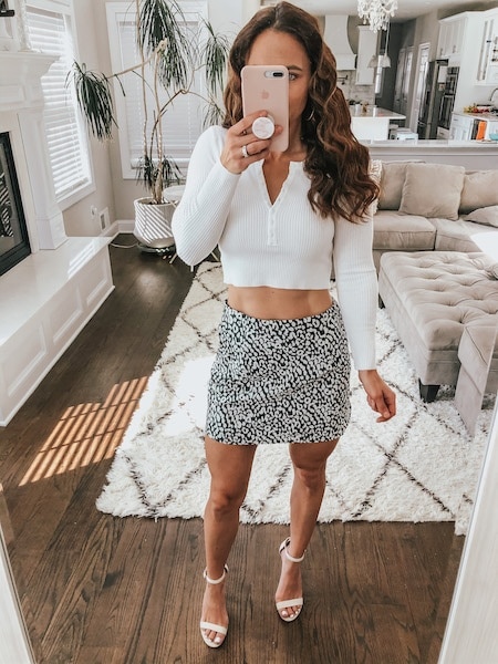 A woman wearing a white long sleeve crop top and a leopard mini skirt.