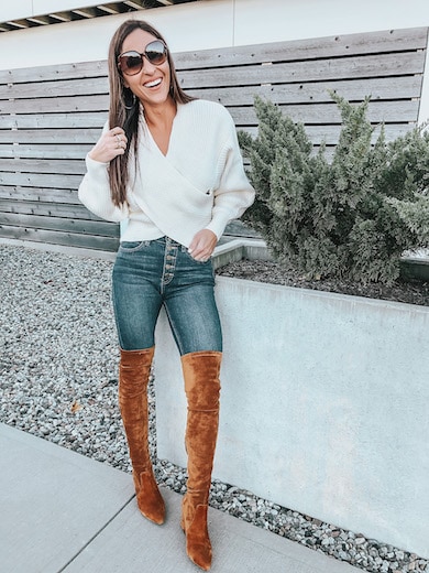 A woman wearing a white sweater and brown over the knee boots.