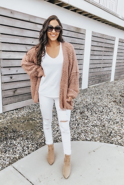 a woman wearing a pink cardigan, white jeans, a white tank top, and tan booties
