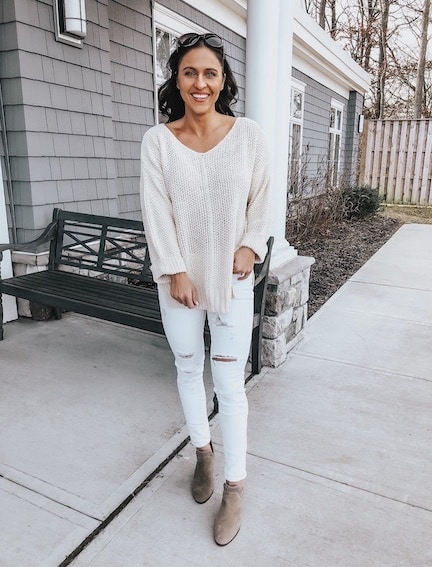 a woman wearing a cream sweater, white jeans, and tan booties