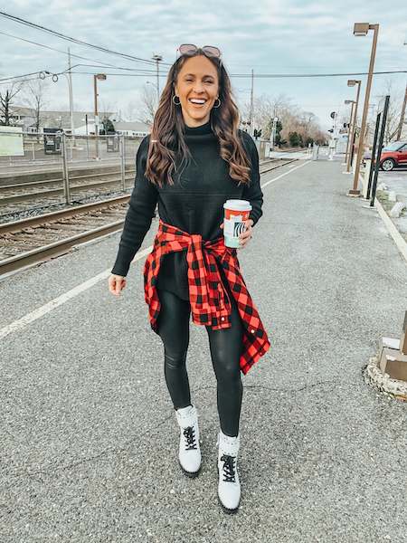 a woman wearing black leggings, a black sweater, white combat boots, and a red flannel tied around the waist