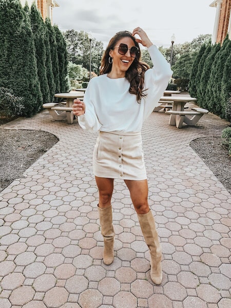 A woman wearing a white sweater and tan mini skirt with tan knee high boots.