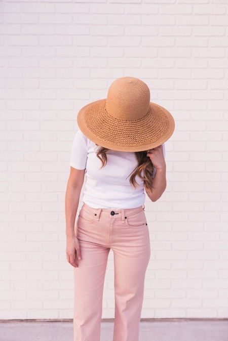 A woman wearing a white shirt and pink pants with an oversized hat.