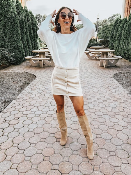 A woman wearing a white swerater, tan knee high boots and a tan mini skirt.