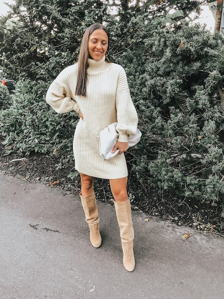 A woman wearing ribbed sweater dress and knee high boots.