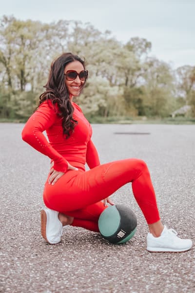 woman wearing a red workout set ad crouching next to a workout ball
