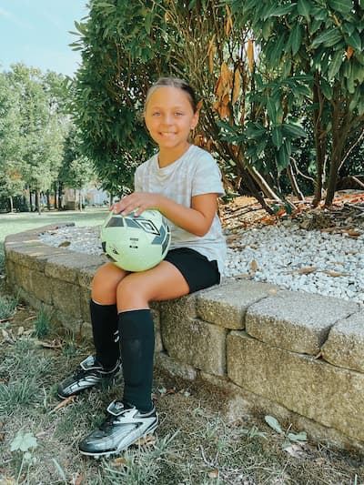 girl sitting with a soccer ball wearing cleats