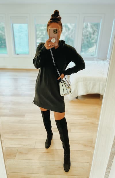 a woman wearing a black sweatshirt dress with black over the knee boots