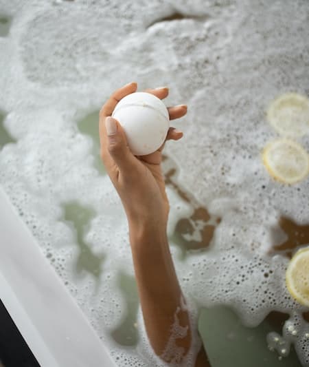 person holding a white bath bomb in a tub
