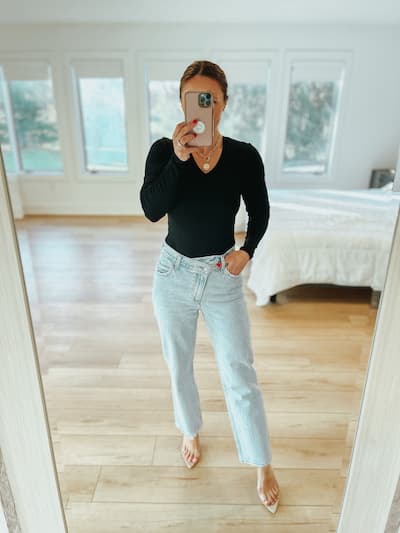 woman wearing a black bodysuit, light wash jeans, and high heels