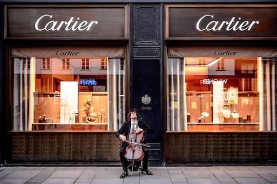 A man outside of the Cartier store playing the viollin.