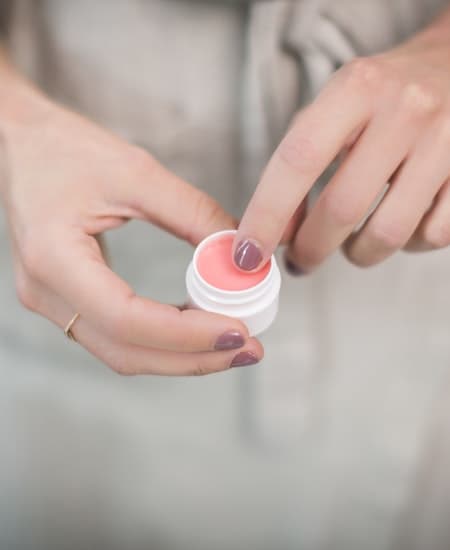 A woman putting her finger in lip balm.