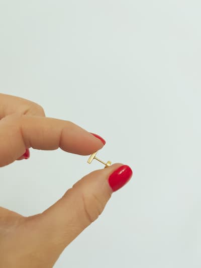 A woman with red nails holding a gold flat back earring.