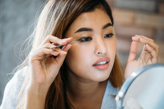 woman using fake eyelash glue to put on eyelashes
