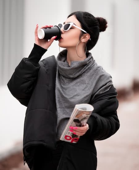 A woman wearing hoop earrings and drinking a coffee.