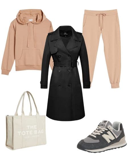 Women's trench coat outfit idea featuring a black trench coat, tan hoodie, tan joggers, neutral sneakers, and a neutral tote bag.