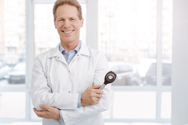 A doctor in a white coat holding a dermatoscope