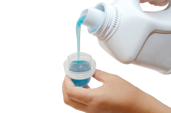 A person pouring laundry detergent into a small cup.