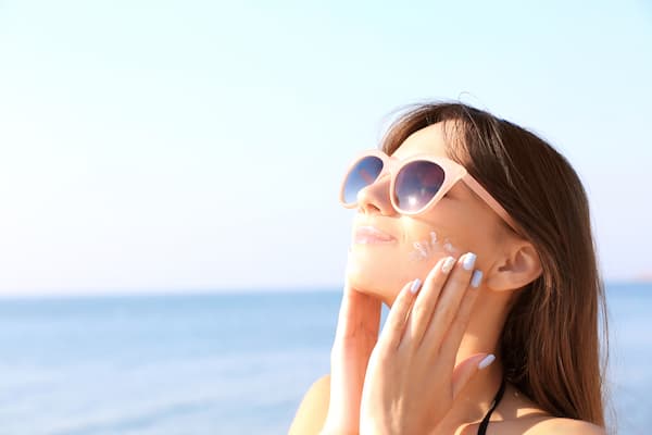 A woman at the beach applying sunscreen to her face.