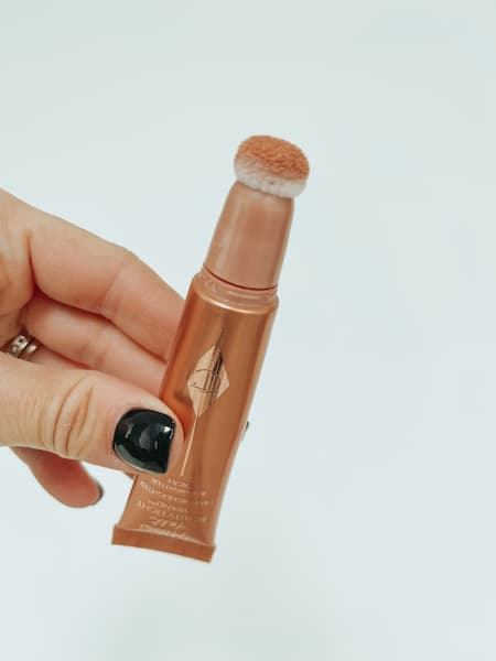 A woman holding the Charlotte Tilbury beauty highlighter wand.