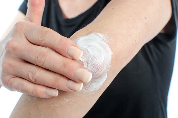 A woman putting lotion on her elbow.