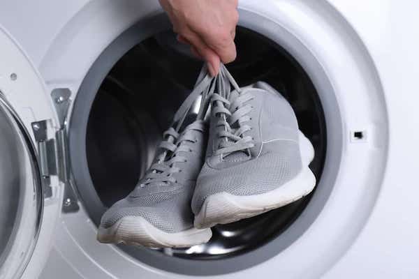 A woman putting a pair of grey sport sneakers into a dryer.