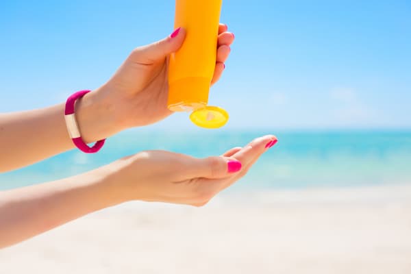 A woman putting sunscreen into the palm of her hand.