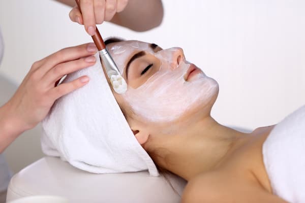 A woman having a white mask applied to her face during a facial.