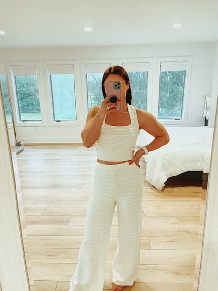 A woman wearing an ivory 2 piece knit set with a crop top and pants.