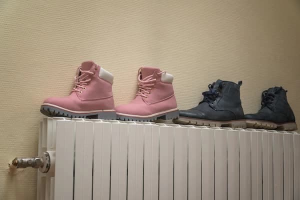 Pink and grey boots drying on a heater.