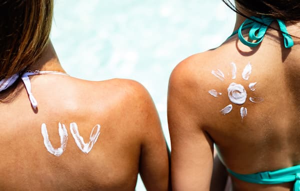 The backs of two women with sunscreen on their shoulders in cute designs.