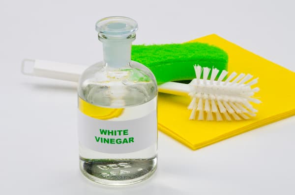 White vinegar next to a brush and sponge.