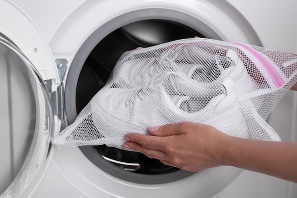 A woman putting white sneakers in a mesh bag into a washing machine.