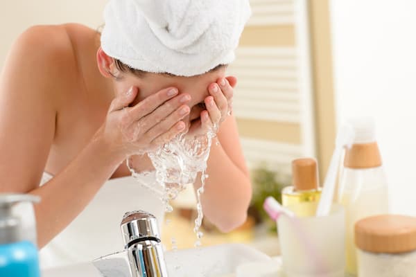 A women washing her face in the sink with a towel on her hair.