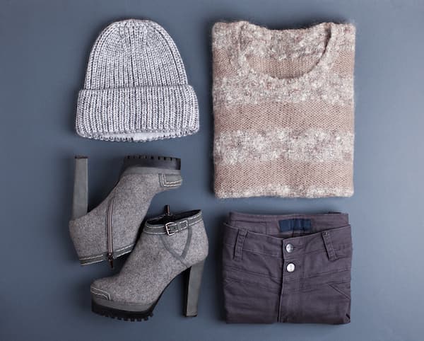 A flatlay of womens clothing incluing a hat, booties, pants, and a sweater.