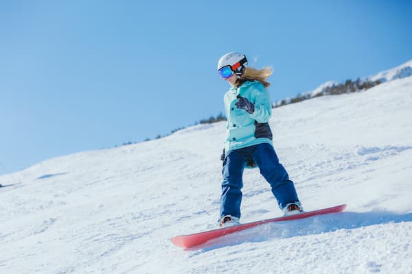A woman in blue ski pants and a teal snow jacket snowboarding down a mountain.jpg