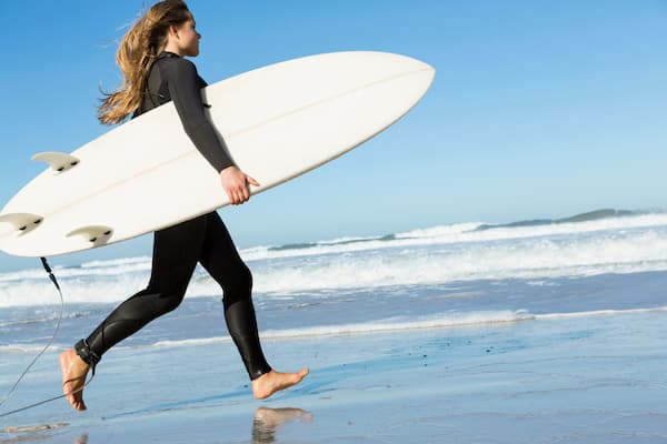 A woman wearing a wetsuit running into the ocean with a surfboard.