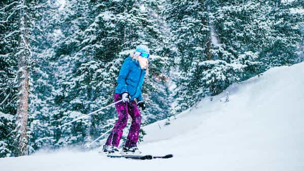 A woman skiing in purple ski pant and a blue ski jacket.