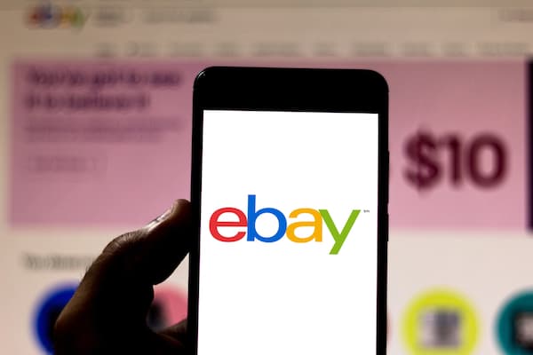 A person holding a mobile phone with the ebay logo on the screen.